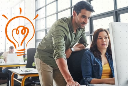 Two colleagues collaborating on a computer in an office, with an orange lightbulb graphic symbolizing a new idea.